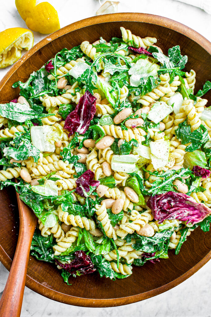 Overhead view of a round dark wood bamboo bowl full of creamy vegan lemon pasta salad