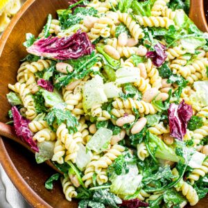 Overhead view of a round dark wood bamboo bowl full of creamy vegan lemon pasta salad