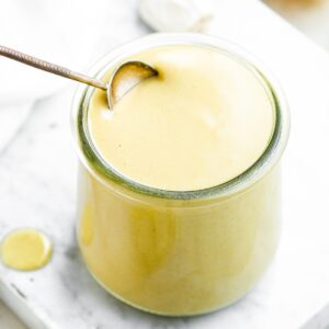 Overhead view of a spoon diving into a glass jar filled with creamy vegan lemon dressing with sliced lemons behind it