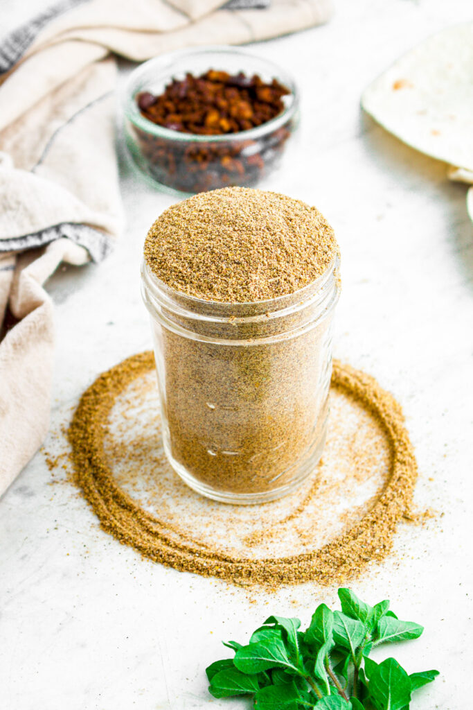 Overhead view of a clear glass jar of vegan taco seasoning with some spilling out creating a circle around the jar