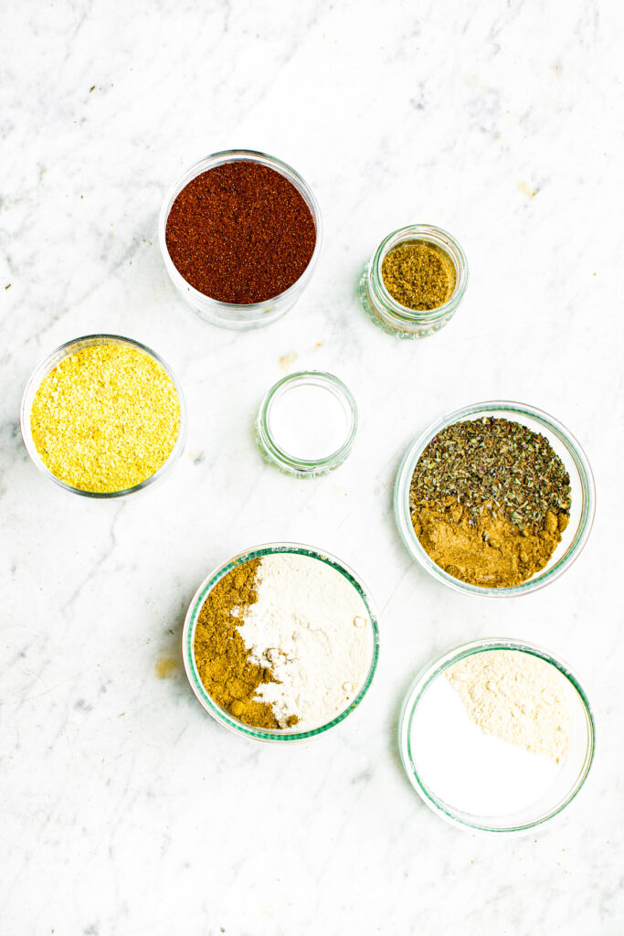 Overhead view of aa variety of spices and dried herbs arranged in clear glass bowls on a grey marble countertop