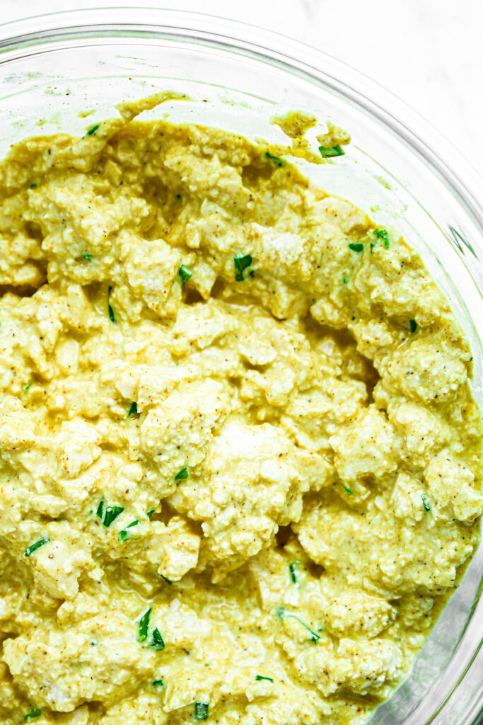 Close up overhead view of a creamy vegan egg salad in a clear bowl with chopped green onions