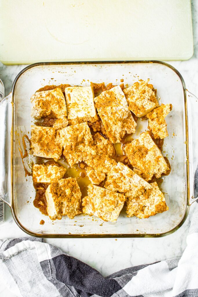 overhead view of a clear square glass baking dish filled with tofu wings marinating in BBQ tofu wing marinade