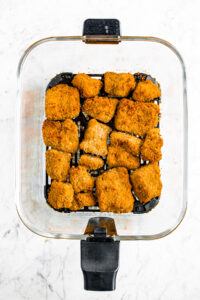 overhead view of a clear glass air fryer jar filled with crispy tofu wings