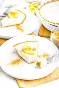 Overhead view of a round white plate with a slice of creamy vegan lemon pie topped with a slice of lemon and graham cracker crumbs