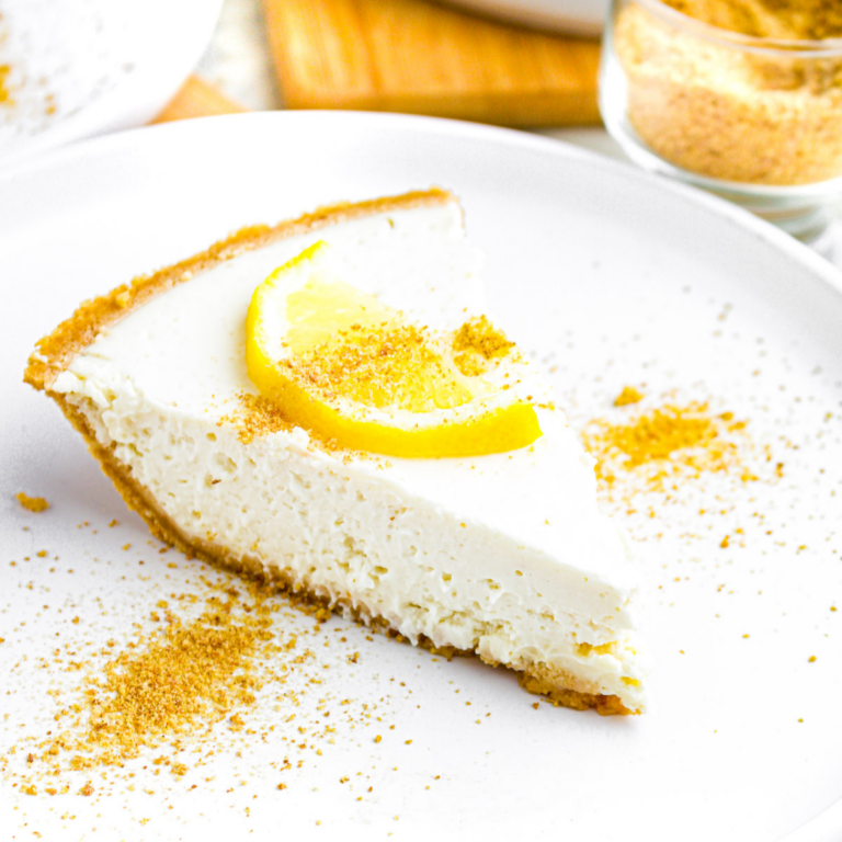 Overhead view of a round white plate with a slice of creamy vegan lemon pie topped with a slice of lemon and graham cracker crumbs