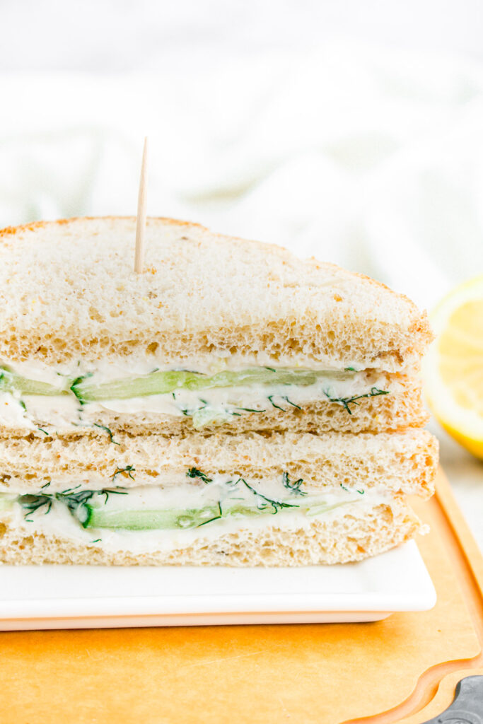 Head on view of a cucumber sandwich sliced in half and stacked on top of each other on a wood cutting board