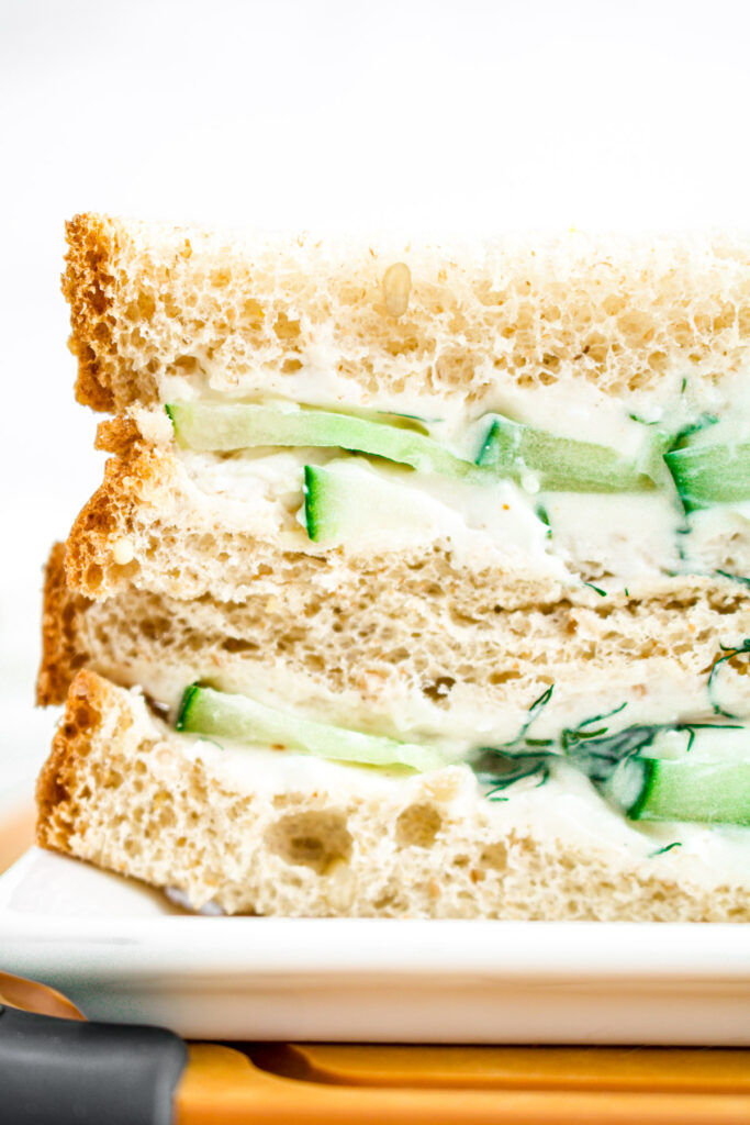 Head on view of a vegan cucumber sandwiches sliced in half and stacked on top of each other on a wood cutting board