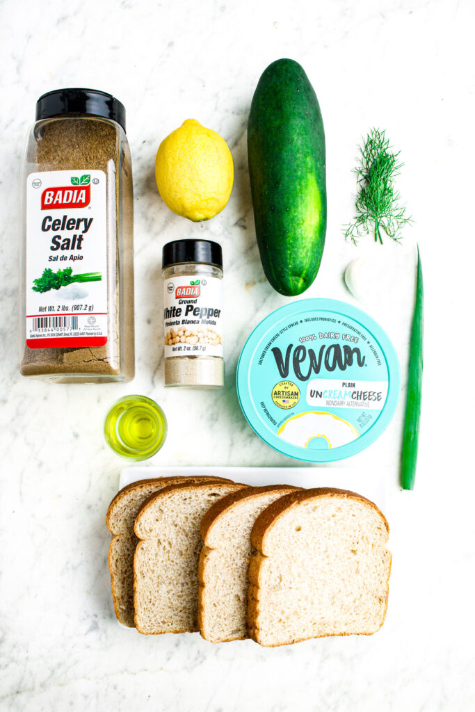 Overhead view of all the ingredients you need to make vegan cucumber sandwiches laid out on a grey marble countertop