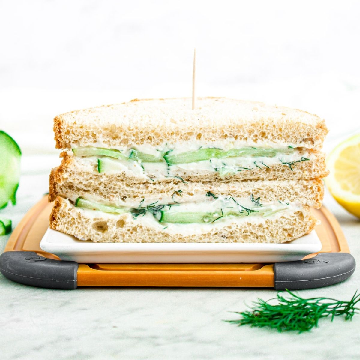 Head on view of a vegan cucumber sandwich sliced in half and stacked on top of each other on a wood cutting board