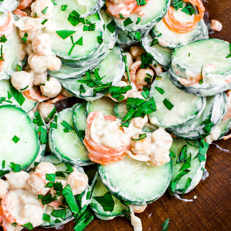Overhead view of a bamboo salad bowl filled with vegan cucumber salad in a creamy lemon dressing with chickpeas and carrot ribbons