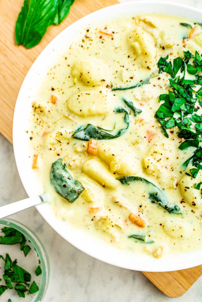 Head on close up view of a round white bowl filled with a creamy dairy-free gnocchi soup topped with minced herbs