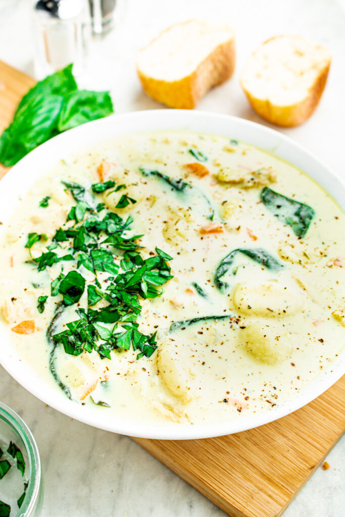 Overhead view of a round white bowl filled with copycat Olive Garden soup in a creamy coconut broth with two slices of bread next to the bowl