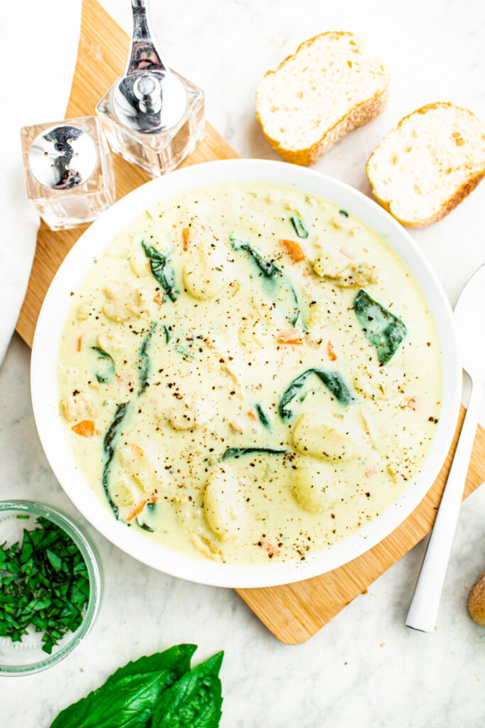 Overhead view of a round white bowl filled with creamy vegan gnocchi soup with fresh basil