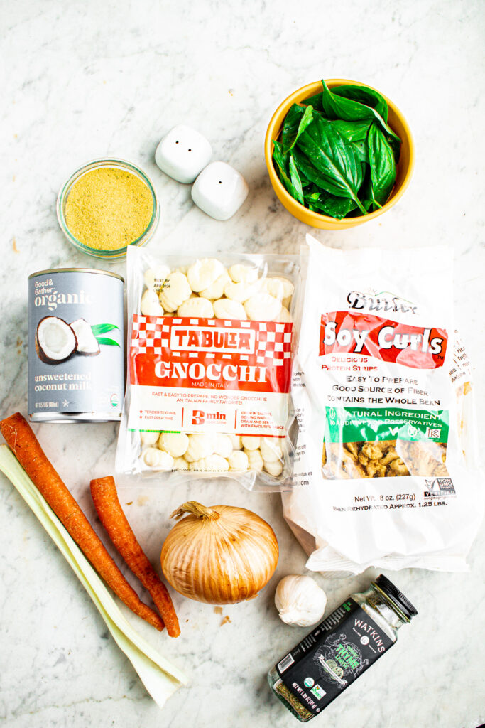 Overhead view of all the ingredients you need to make creamy vegan gnocchi soup laid out on a grey marble countertop