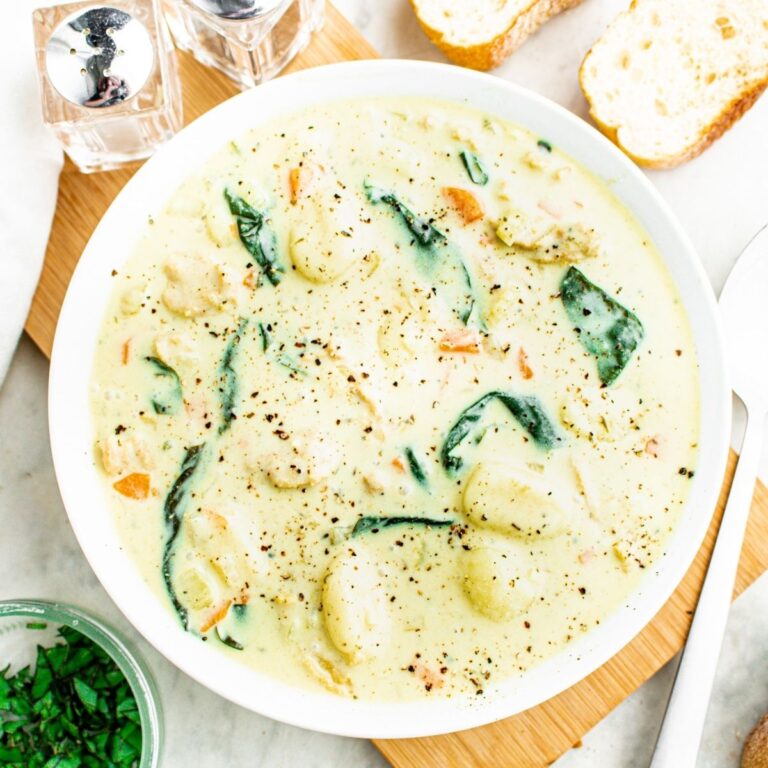 Overhead view of a round white bowl filled with creamy vegan gnocchi soup with fresh basil