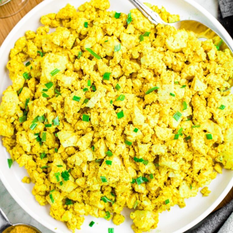 Overhead close up view of a round white plate piled high with tofu scramble topped with minced green herbs