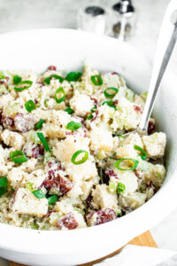 Overhead view of a round white bowl filled with vegan potato salad made with red potatoes topped with chopped scallions