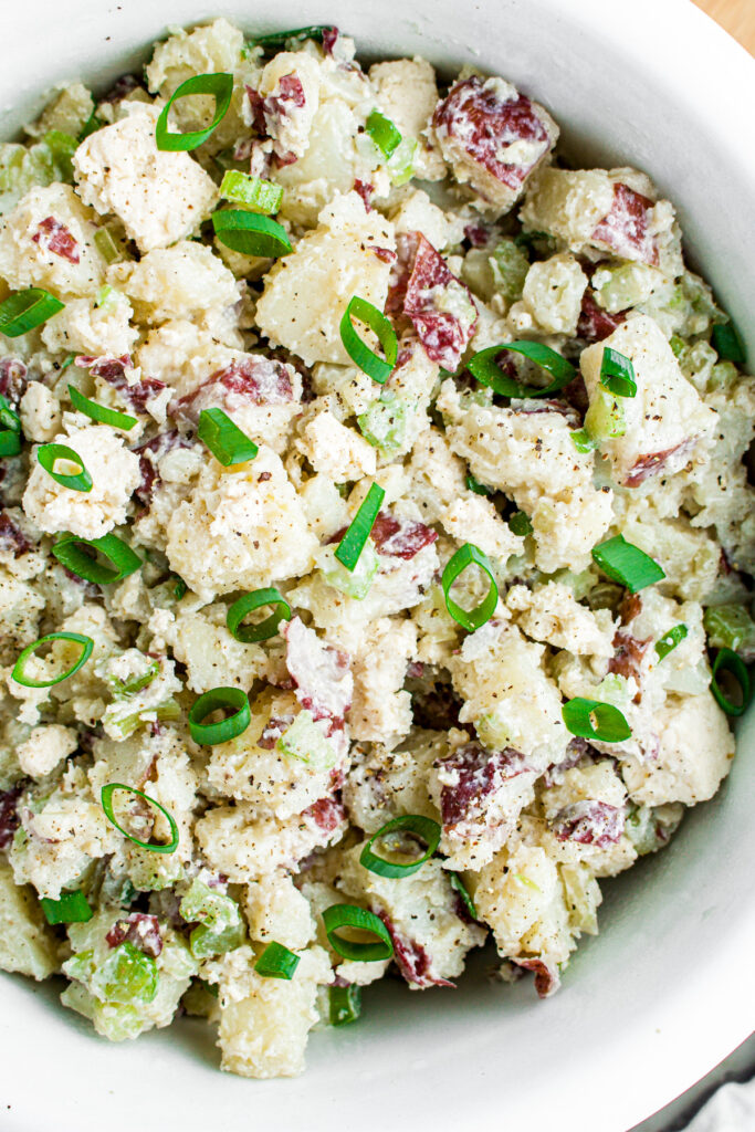 Overhead zoomed in view of a round white bowl filled with creamy dairy free potato salad topped with chopped green onions