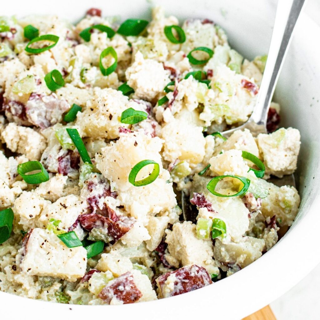 Overhead close up view of a round white bowl filled with vegan potato salad made with red potatoes topped with chopped scallions