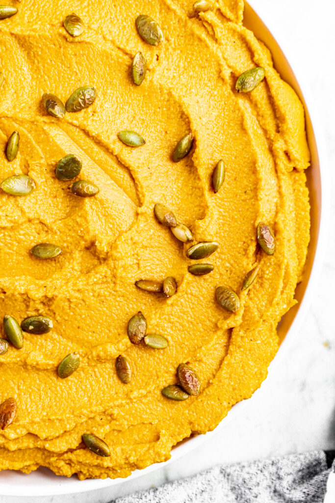 Overhead view of a round white plate with a schmear of whipped vegan pumpkin ricotta topped with toasted pepitas