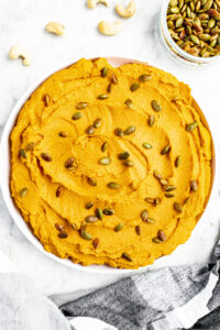 Overhead view of a round white plate with a schmear of whipped vegan pumpkin ricotta topped with toasted pepitas