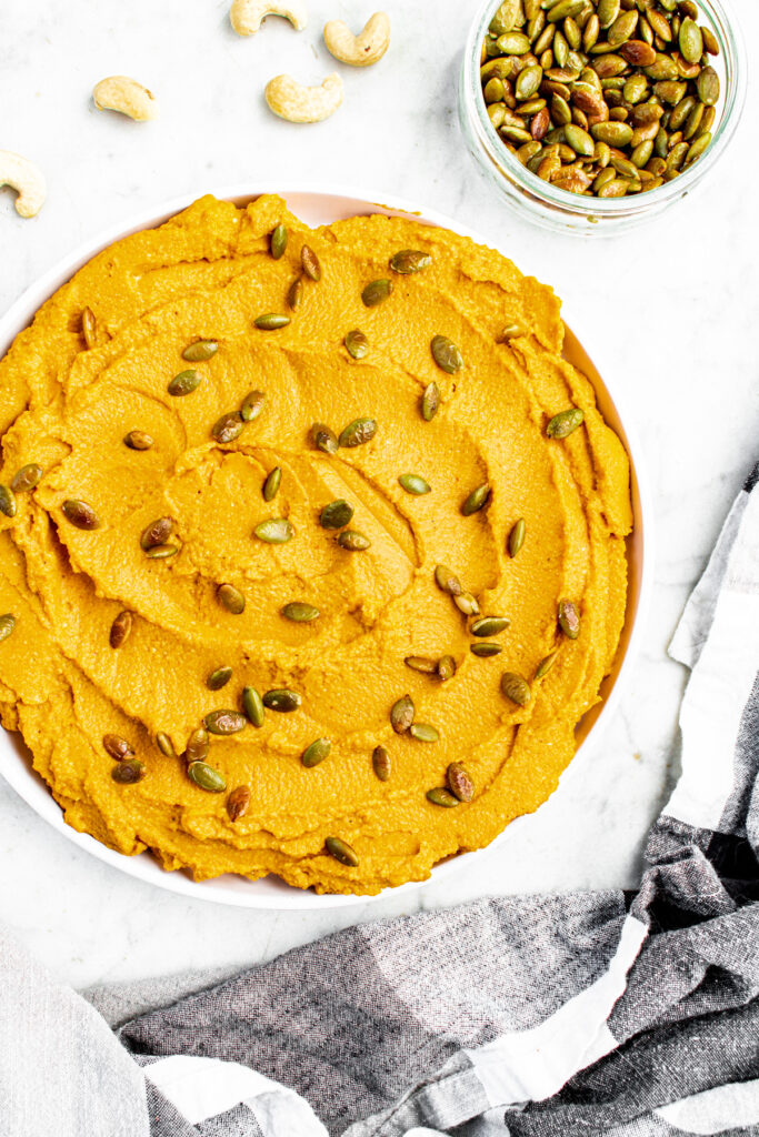 Overhead view of a round white plate with a schmear of whipped vegan pumpkin ricotta topped with toasted pepitas