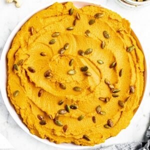 Overhead view of a round white plate with a schmear of whipped vegan pumpkin ricotta topped with toasted pepitas