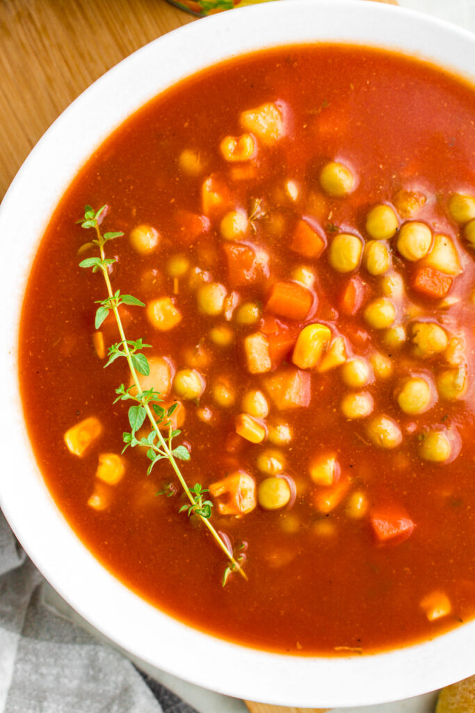 Overhead close up view of a round white bowl filled with v8 vegetable soup with a sprig of thyme on one side