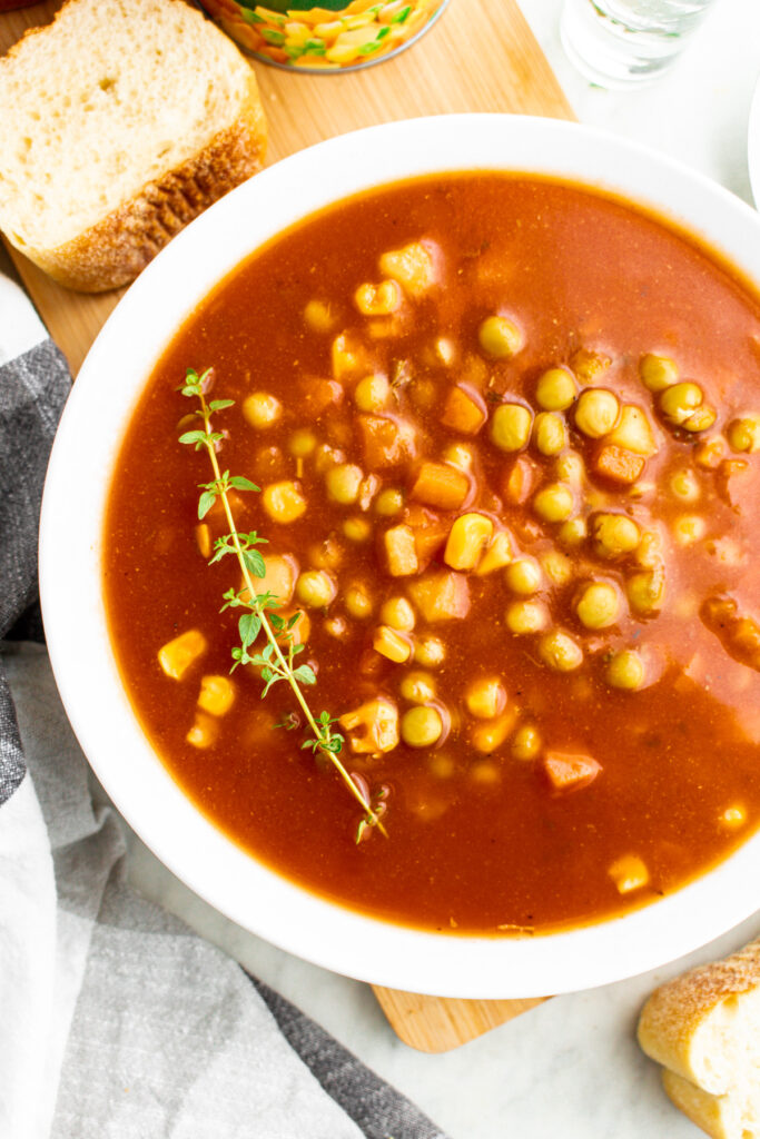 Overhead close up view of a round white bowl filled with v8 vegetable soup with a sprig of thyme on one side