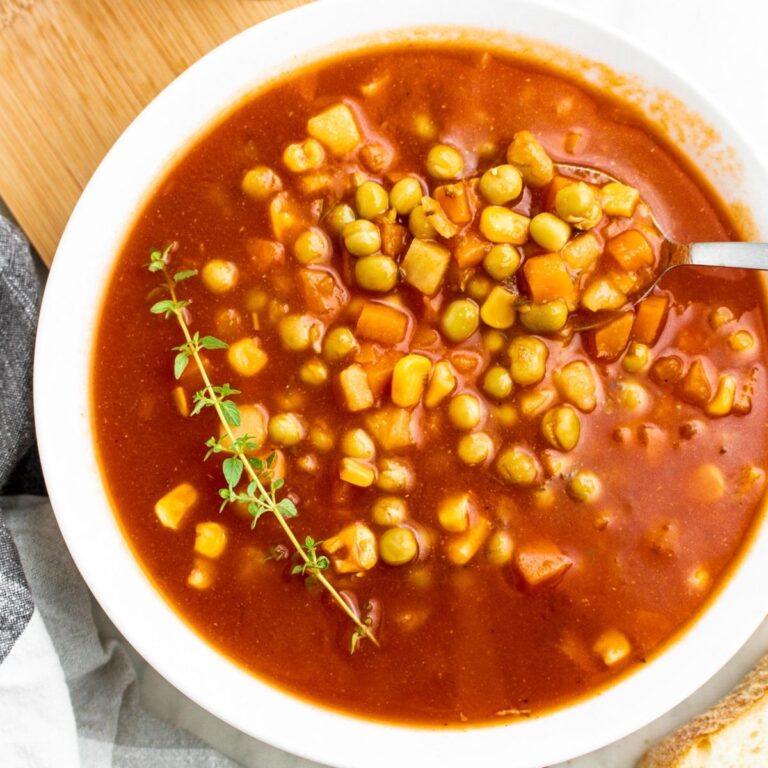 Overhead view of a round white bowl filled with v8 vegetable soup with a sprig of thyme on one side and a spoon digging into the other side