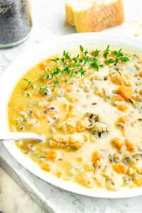 Overhead view of a round white bowl filled with creamy vegan wild rice soup with a spoon digging into it