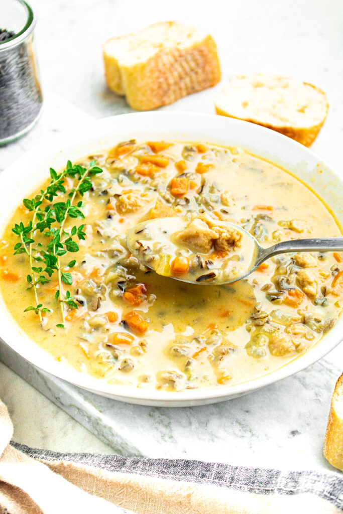 Overhead view of a round white bowl filled with creamy vegan wild rice soup with a spoon digging into it