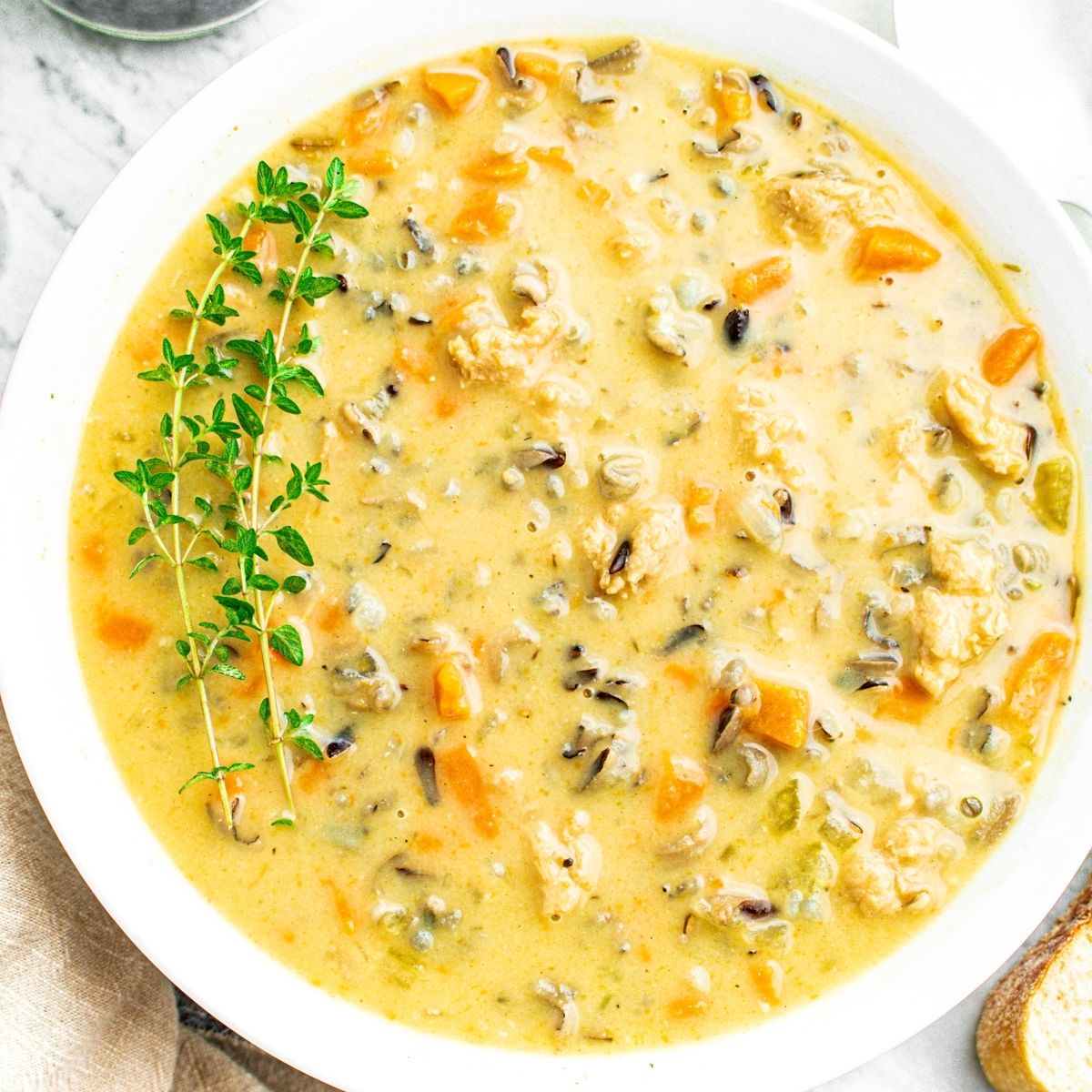 Overhead view of a round white bowl filled with creamy vegan wild rice soup with a sprig of thyme in the upper left corner