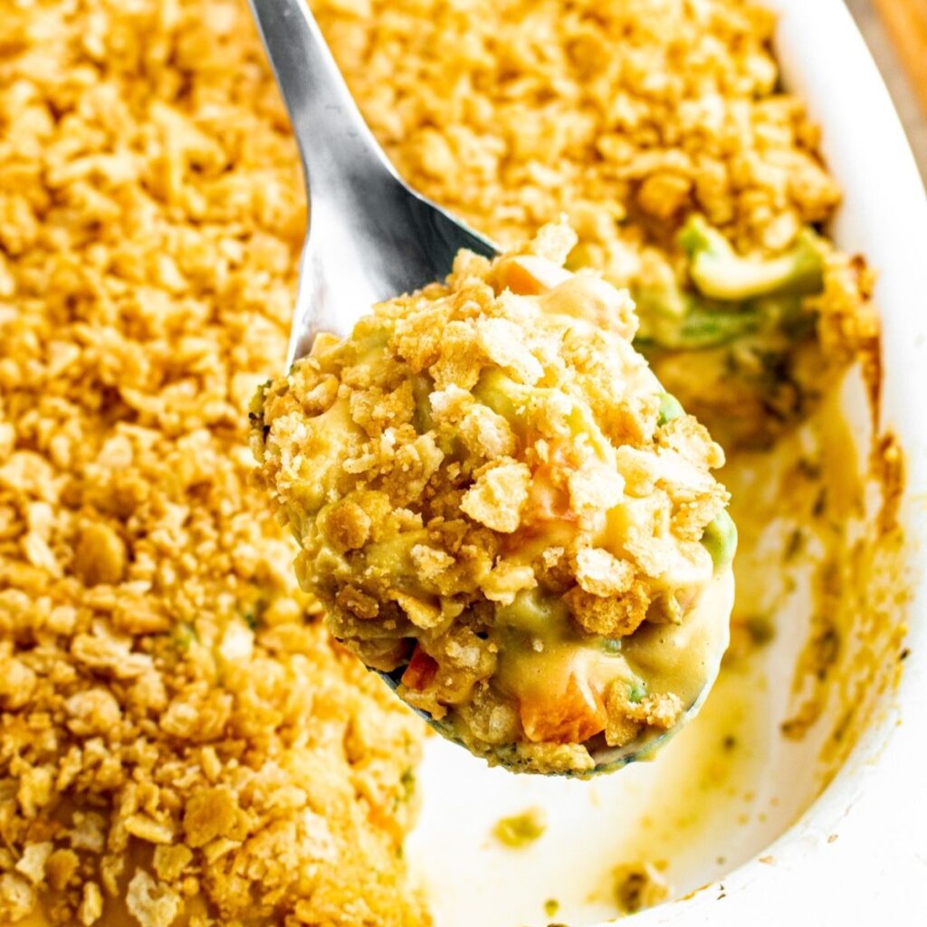 Overhead view of a large silver spoon scooping up some cheesy vegan vegetable casserole from the casserole dish