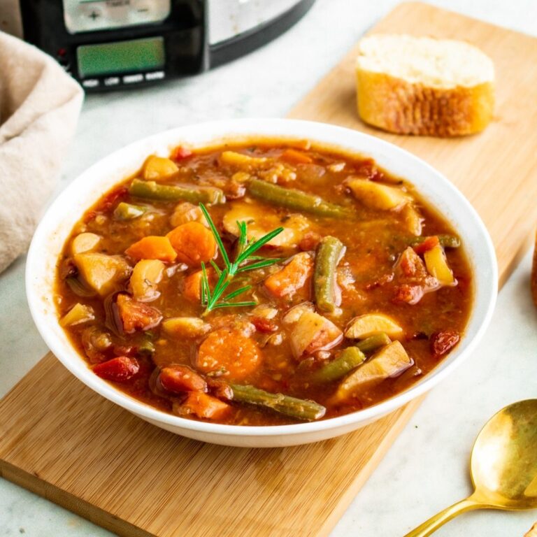 Overhead view of a round white bowl filled with thick vegetable stew with a slow cooker in the background