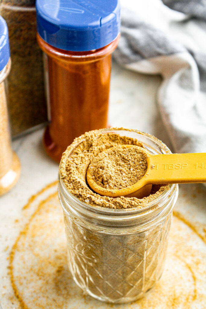 Overhead view of a clear glass jar filled with homemade vegan beef bouillon powder with a Tbsp digging into it and broth powder spilling over the edges