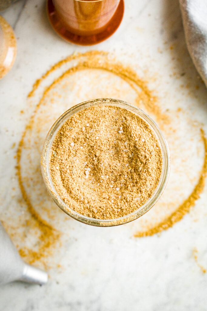 Overhead view of a clear glass jar filled with homemade vegan beef bouillon powder with broth powder spilling over the edges