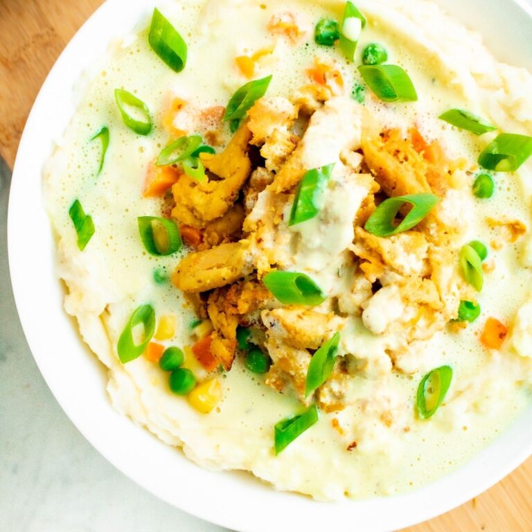 Overhead close up view of a round white bowl filled with a creamy vegan mashed potato bowl with veggies, soy curl chicken, and creamy cashew gravy