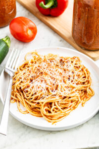Overhead view of a round white plate piled high with spaghetti in a hidden vegetable sauce topped with vegan parmesan