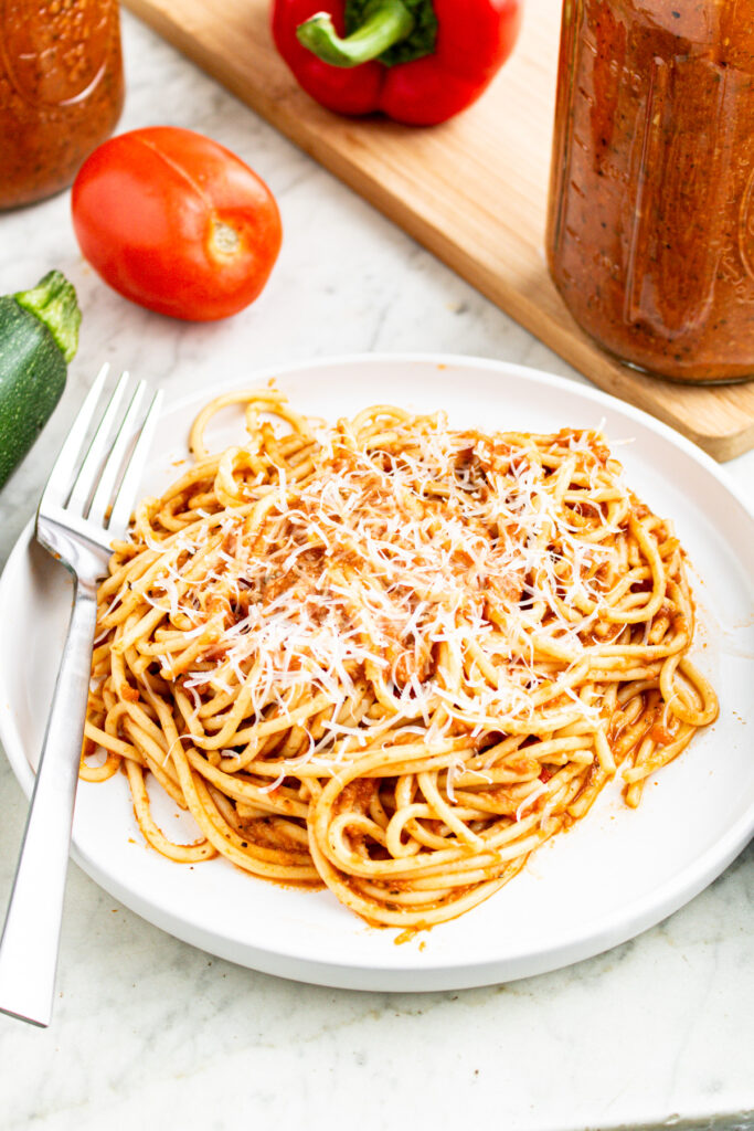 Overhead view of a round white plate piled high with spaghetti in a hidden vegetable sauce topped with vegan parmesan