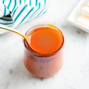 Overhead view of a clear glass jar filled with creamy vegan buffalo sauce with a gold spoon digging into it
