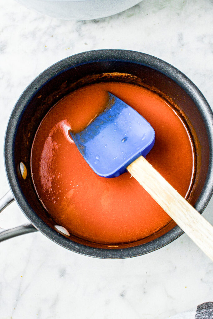 Overhead view of a small black saucepan filled with creamy vegan buffalo sauce with a blue spatula stirring it