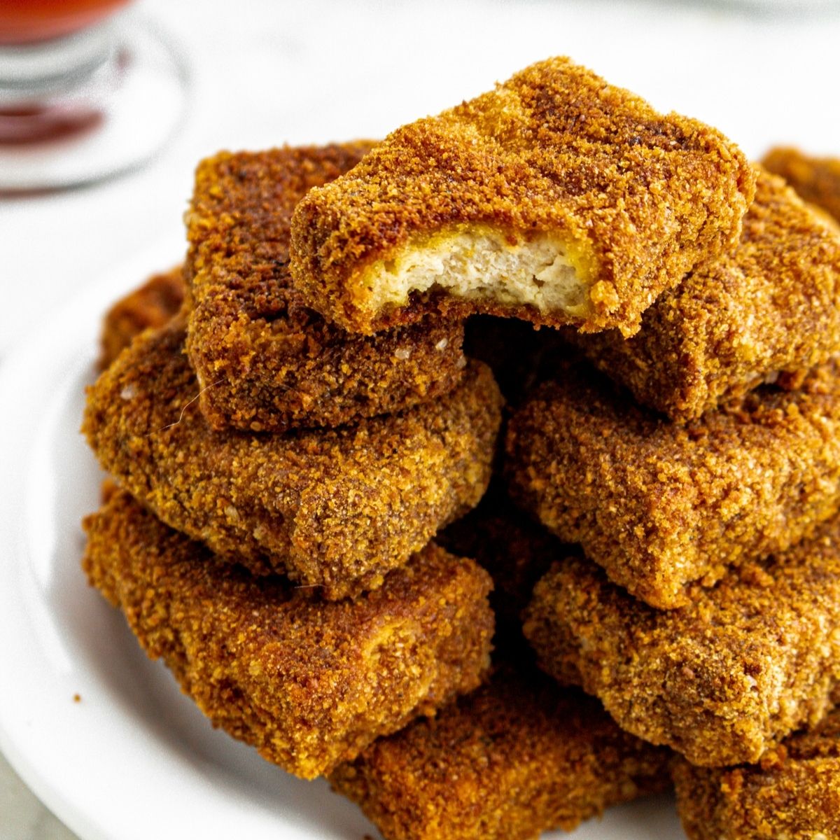 Overhead view of a round white plate piled high with tofu nuggets with a bite taken out of the top one
