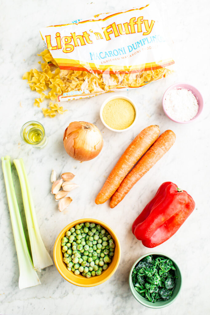 Overhead view of all of the ingredients to make vegetable noodle soup laid out on a grey marble countertop