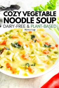Overhead view of a round white bowl filled with vegetable noodle soup with celery behind the bowl, red pepper in front of it, and text reading cozy vegetable noodle soup dairy free and plant based