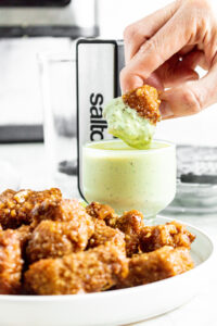Head on view of a hand dipping a pineapple tofu wing into a creamy avocado ranch dip