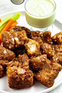 Overhead close up view of a pile of pineapple tofu wings on a round white plate with a bite taken out of the top one