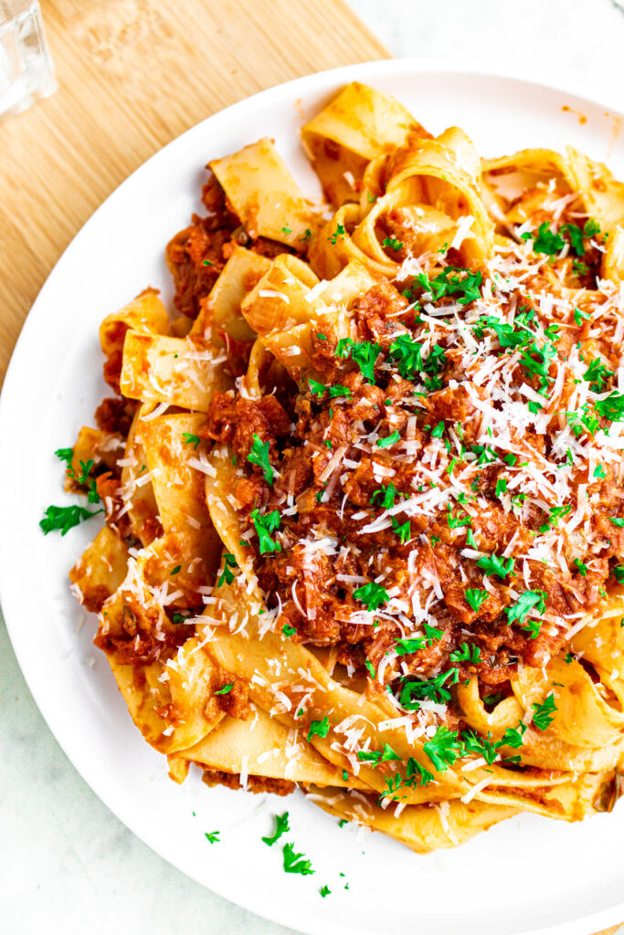 Overhead view of a round white plate with a pile of wide noodles in vegan bolognese topped with green herbs