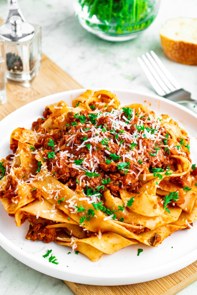 Overhead view of a round white plate topped with a large swirl of vegan bolognese noodles topped with fresh minced herbs
